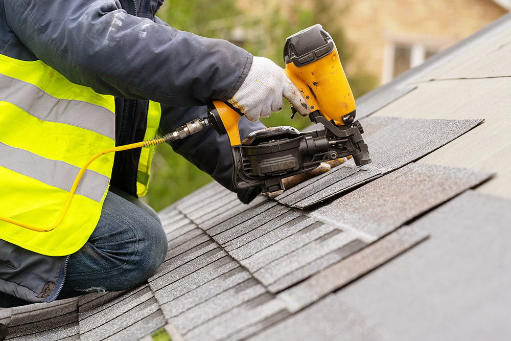 A construction worker installing roof shingles with a nail gun